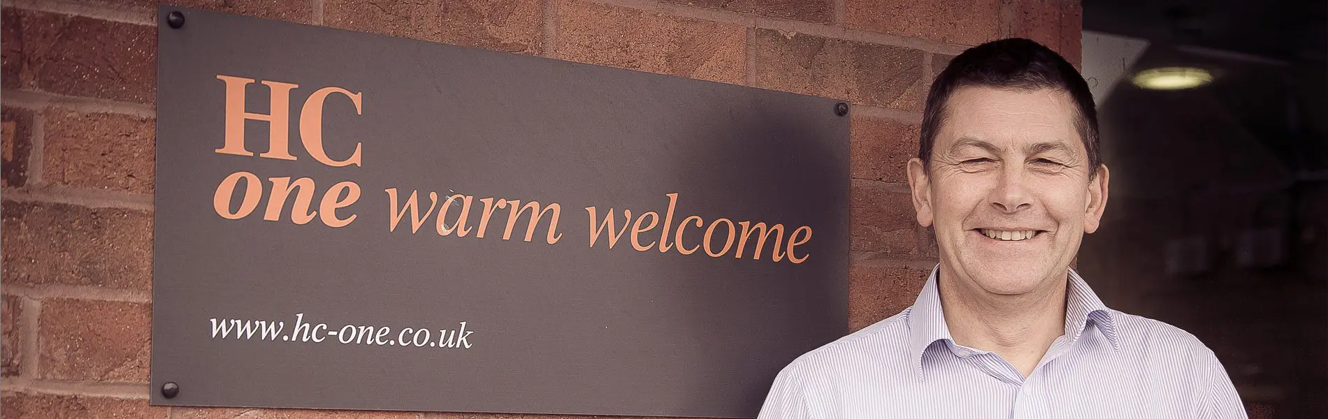 An individual standing in front of a HC-One logo sign.