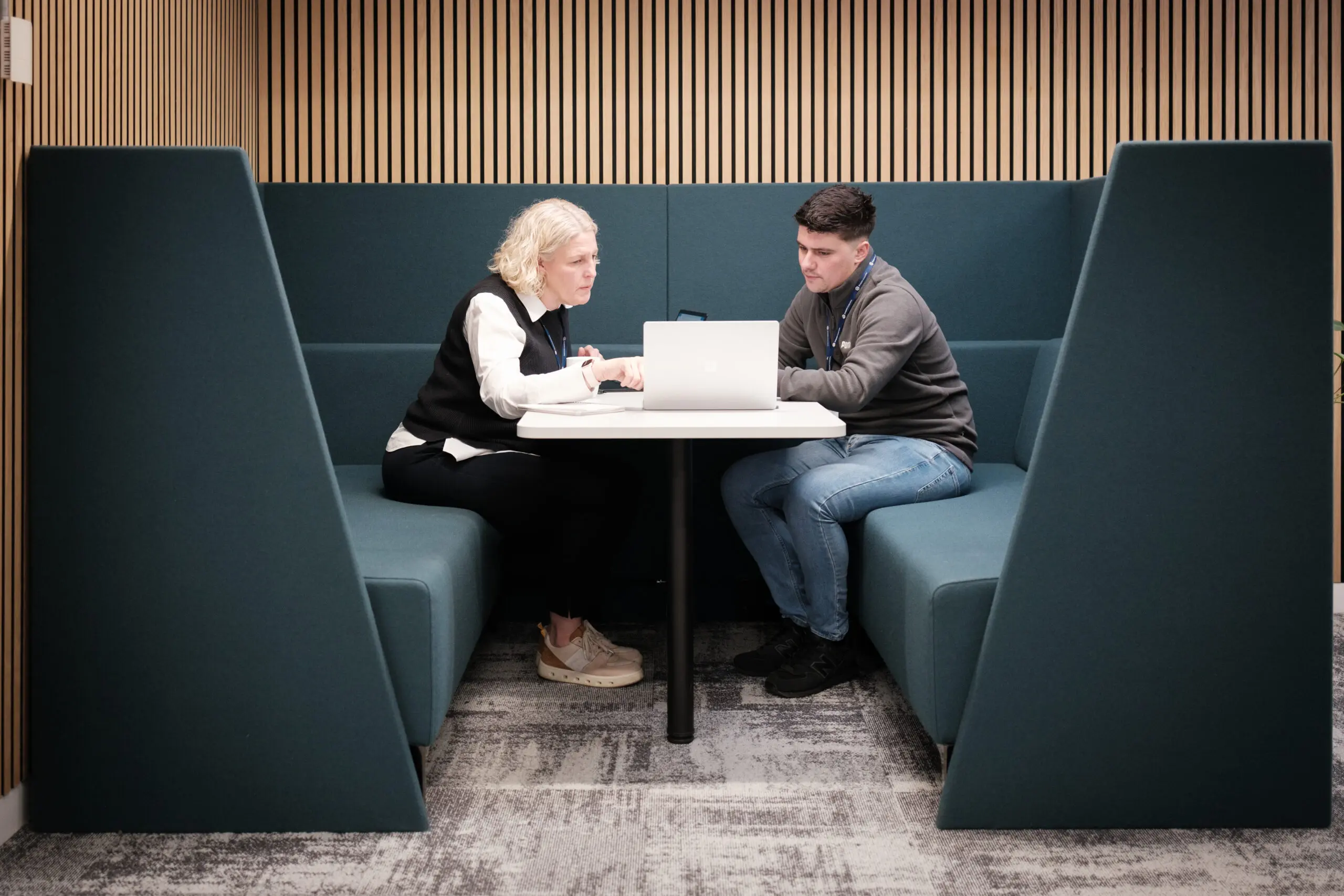 two team members sat across from each other with a laptop inbetween them.