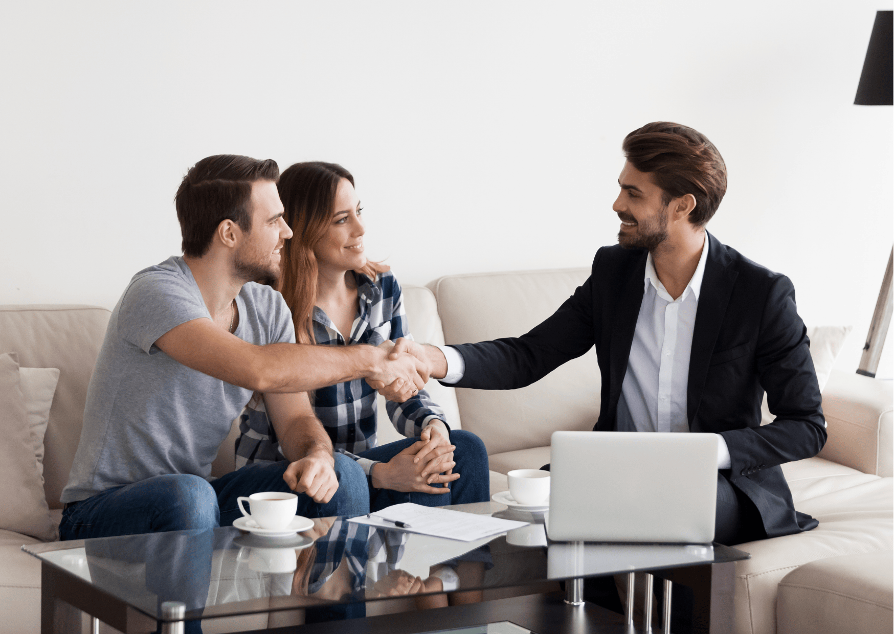 a couple, sat on a sofa, shaking hands with a business man 